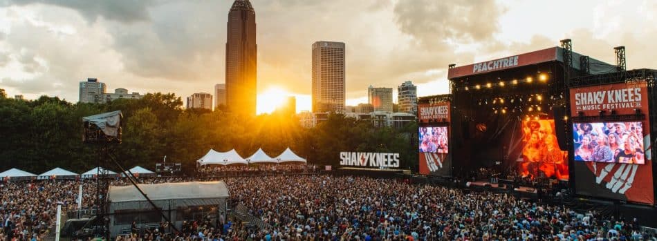 Shaky Knees festival picture of the event stage and crowd in the foreground with the setting sun behind the city skyline in the background